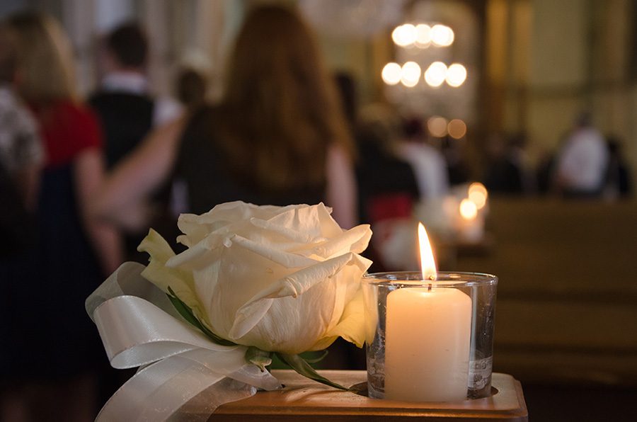 A white rose and a white candle as funeral arrangement in a church